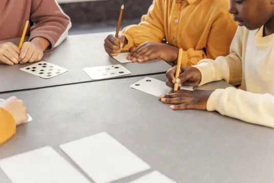 Diverse group of students at a table calculating card probabilities with pencils, paper, and playing cards spread out