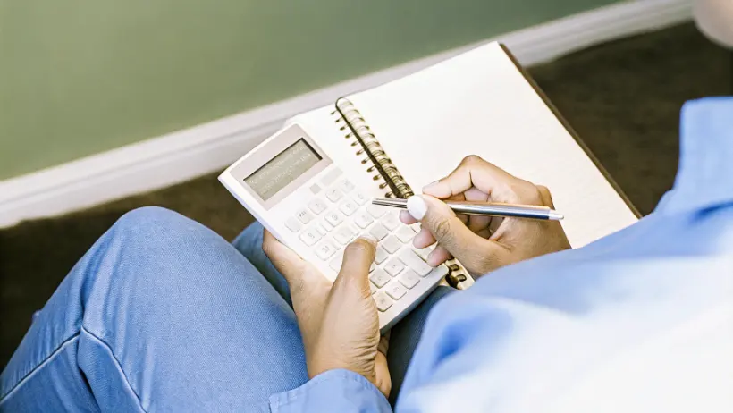 Person using calculator and notebook for budget planning