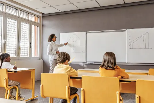 Teacher standing at whiteboard with dice and probability graphs while students take notes in modern classroom